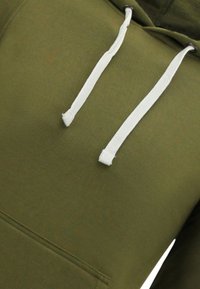 Olijfgroene hoodie met witte trekkoorden, een voorzak en een zachte, textuurachtige stof. Gestikte naden zijn zichtbaar langs de randen.