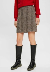 Hnědá sukně s kostkovaným vzorem vyrobená z texturované látky, doplněná černými kozačkami po kolena se zelenými podrážkami. Na vrchu je červený svetr.