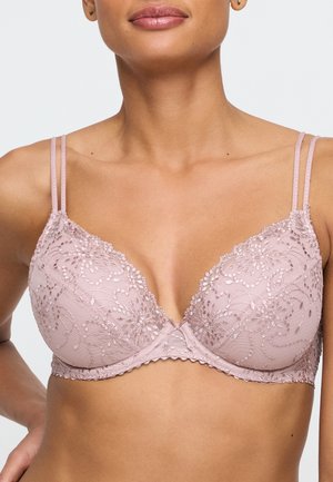 Femme portant un soutien-gorge en dentelle mauve clair avec broderie florale et bretelles doubles, montrant le haut du torse et le cou.