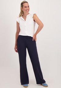 Witte blouse met korte mouwen en knoopsluiting, gecombineerd met marineblauwe wijde broek. De schoenen zijn lichtblauw met een gestructureerd oppervlak.
