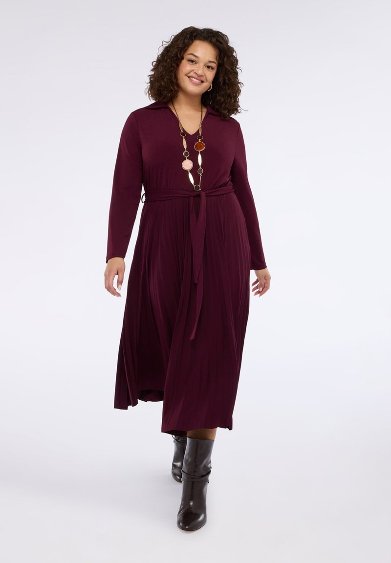 Bordowa sukienka z długim rękawem, kołnierzykiem, plisowaną spódnicą i wiązaniem w talii. Stylizowana z wysokimi, brązowymi, luźnymi botkami na obcasie oraz warstwowym naszyjnikiem.