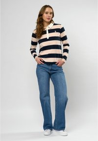Lange mouw polo met marineblauwe en lichtroze strepen, witte kraag en logo. Gecombineerd met lichtblauwe flare jeans en witte sneakers.