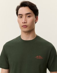 Πράσινη βαμβακερή μπλούζα με στρογγυλή λαιμόκοψη και κοντά μανίκια. Διαθέτει ένα μικρό κόκκινο λογότυπο στην αριστερή πλευρά του στήθους. Λείο υλικό.