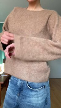 Bežový vlnený sveter so širokými rukávmi, vo voľnom strihu a s jemnou textúrou, skombinovaný s svetlomodrými džínsami.