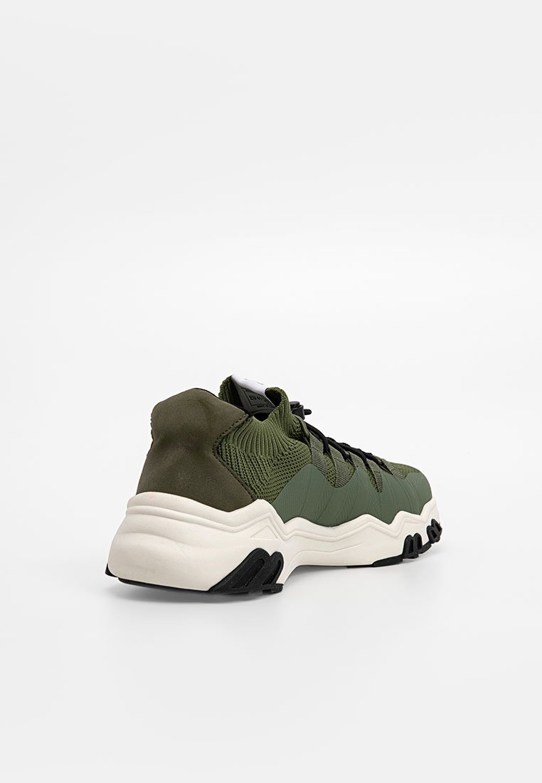 Grüner Mesh- und Wildledersneaker mit strukturiertem Obermaterial und schwarzen Akzenten. Verfügt über eine klobige weiße Sohle und ein kontrastierendes schwarzes Außensohlen-Design.