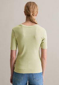 Lichtgroen geribbeld T-shirt met korte mouwen en een wijde halslijn. Draag het met hoogwaist blauwe denim jeans. Eenvoudig ontwerp zonder zichtbare patronen.