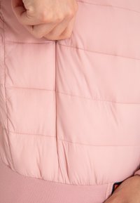 Jasnoróżowa kurtka puchowa z poziomym pikowaniem, gumowym akcentem w pasie oraz zapinaną na zamek kieszenią na klatce piersiowej.