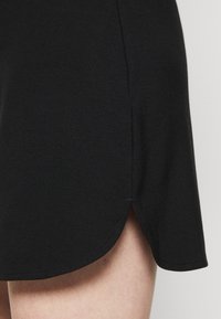 Černá bavlněná sukně s rozšířeným lemem a bočním rozparkem, která se vyznačuje hladkou texturou a jednoduchým designem, podtrhující jednoduchost stylu.