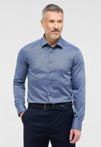 Blauwe overhemdoom met een gestructureerd patroon, lange mouwen en donkere knopen, gecombineerd met marineblauwe broek en een geweven zwarte riem.