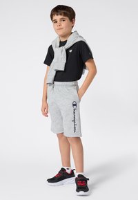 Czarny T-shirt, szare spodenki z logo i czarne sneakersy z czerwonymi akcentami. Szara bluza zarzucona na ramionach, casualowy strój sportowy.