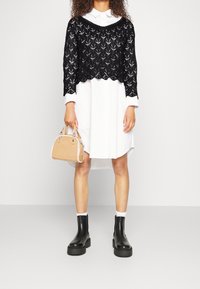 Svart spetsoverdel i kort modell över en vit skjortklänning, matchad med en beige handväska och svarta ankelstövlar med tjock sula.