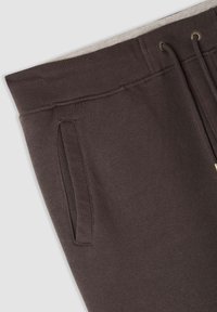 Pantaloni sportivi marrone scuro con vita a costine, due tasche laterali e un laccio. Texture morbida e sottile dettaglio di cucitura a contrasto.
