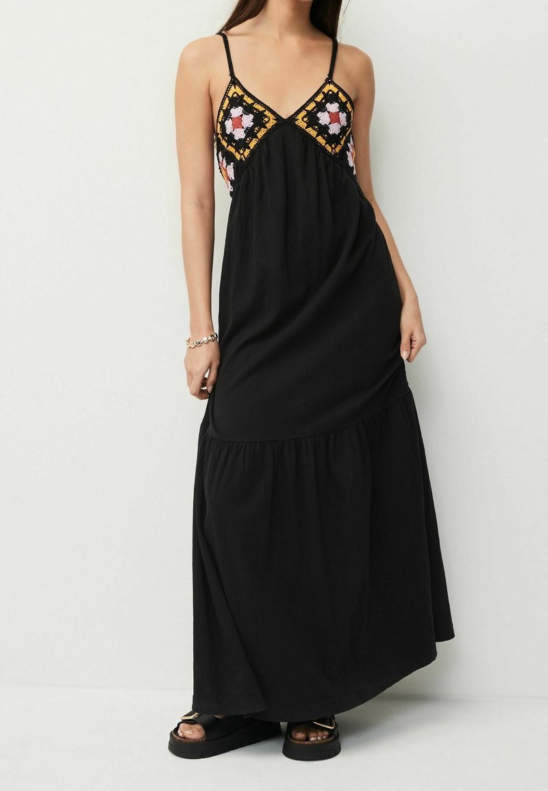Robe maxi noire à fines bretelles, décolleté en V, et corsage brodé coloré présentant des motifs floraux et géométriques. Texture de jupe fluide.