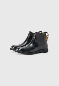 Bottines Chelsea en cuir noir avec une texture lisse, des panneaux latéraux en élasthanne, des détails de brogue décoratifs et une semelle robuste pour une meilleure traction.