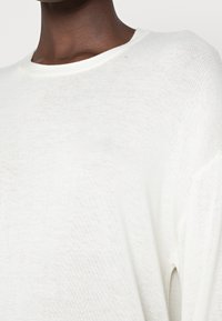 Vit, lätt stickad tröja med avslappnad passform, som har en rund halsringning och mjukt, strukturerat tyg. Synligt sömmönster.