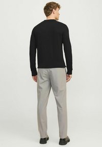 Camisa polo negra de manga larga combinada con pantalones grises claros. El conjunto presenta un diseño simple y clásico con un corte estándar y puños acanalados.