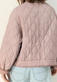 Veste matelassée en tissu rose clair, avec un motif en losanges et des poignets côtelés. Détails de coutures au niveau des épaules et de l'ourlet.