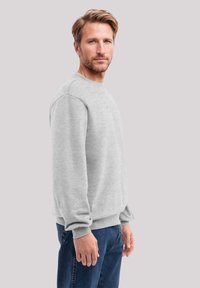 Grauer Sweatshirt mit Rundhalsausschnitt und gerippten Bündchen. Maschinengearbeitete Textur, mit einem lässigen Schnitt. Kombiniert mit blauen Jeans.