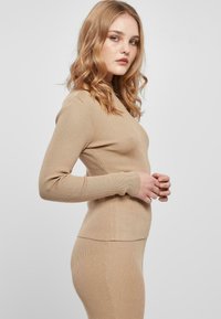 Beige ribbetty knit-pitkähihaisen paidan sopiva malli ja pyöreä kaula-aukko, yhdistettynä yhteensopivaan ribbettä hameeseen. Sujuva pinta ja joustava materiaali.
