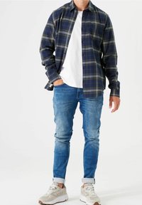 Marinblå rutigt flanellskjorta med gröna accenter, en vit t-shirt med rund hals, slitna blå jeans och ljusgrå sneakers med en kraftig sula.