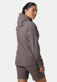 Chaqueta marrón con capucha y mangas largas, combinada con pantalones cortos a juego. La tela parece suave y elástica con un diseño deportivo.