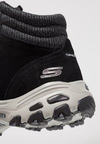 Czarne zamszowe buty trekkingowe z żeberkowym szarym kołnierzem, masywną białą podeszwą z teksturowanym czarnym bieżnikiem oraz metalicznym detalem w kształcie logo "S".