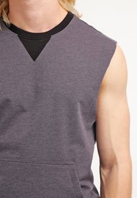 Sudadera sin mangas gris con un escote redondeado y detalles de acento en negro con canalé. Incorpora un bolsillo en la parte frontal y una textura de tela suave.