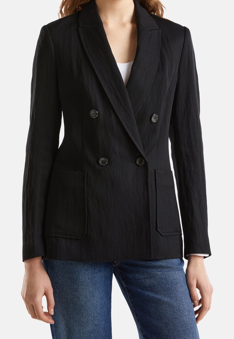 Svart dubbelknäppt kavaj med en texturerad tyg, slagkrage, två framfickor och svarta knappar. Bärs över en vit topp och jeans.