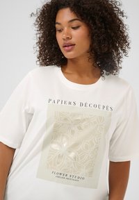 T-shirt en coton blanc avec un imprimé floral en beige clair et or, comportant le texte « PAPIERS DÉCOUPÉS » et « FLOWER STUDIO ». 