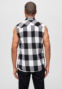 Ujjatlan kockás ing fekete-fehér színben, nagy kockás mintával, gallérral és varrott részletekkel a szélén.