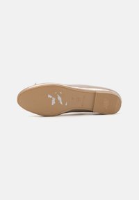 Beige platt skosula som har en slät ljusbrun gummiyta med strukturerade spår och varumärkestryck, något sliten med repor.