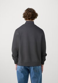 Dunkelgrauer Sweatshirt mit hohem Kragen, gerippten Bündchen und Saum. Kombiniert mit hellblauen Jeans, die eine entspannte Passform und weiche Textur zeigen.