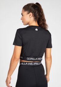 Zwarte cropped t-shirt met korte mouwen, voorzien van een klein wit logo op de achterkant en een gebrandmerkte elastische tailleband aan de onderkant.