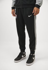 Μαύρο φόρεμα Nike με γκρίζες ρίγες στο πλάι, ελαστικές μανσέτες και λογότυπο. Συνδυασμένο με μαύρα αθλητικά παπούτσια Nike με λευκές λεπτομέρειες.