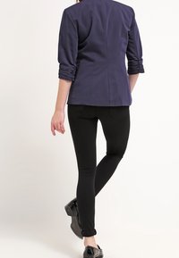 Granatowa marynarka o dopasowanym kroju z marszczonymi rękawami, w połączeniu z czarnymi wąskimi spodniami. Obuwie o błyszczącej powierzchni. Prosta, nowoczesna sylwetka.