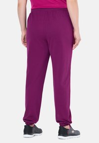 Lila Sporthosen mit einem elastischen Bund, schmal zulaufenden Beinabschlüssen und glatter Textur. Kombiniert mit grauen Sneakern, die einen lässigen Look zeigen.