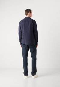 Marineblå lin long-sleeve skjorte med krage, knappemanchetter og en avslappet passform, kombinert med mørkeblå jeans og beige sneakers.