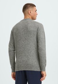 Suéter gris de punto con mangas largas, cuello redondo y dobladillo acanalado. Presenta una tela suave y texturizada. Modelo mostrado de espaldas.