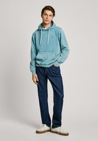 Lichtblauwe hoodie van zachte stof met een voorzak en trekkoorden. Gecombineerd met donkerblauwe jeans en witte sneakers. Eenvoudig ontwerp.