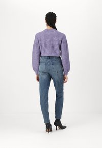 Pull en maille lavande à texture côtelée, associé à un jean bleu taille haute. Des bottines noires à talons complètent la tenue.