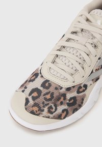 Basket de sport avec une tige en mesh beige arborant un motif léopard marron et noir, avec un capuchon de orteil gris clair et une semelle blanche.