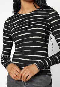 Svart- och vitt randig långärmad topp i ribbat tyg, med rund halsringning och figurnära design, med varierande randbredd.