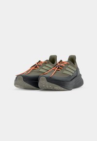 Trailrunningschoenen met een donkergroene bovenkant, een gevoerde zool, oranje veters en het iconische logo met drie strepen. Gestructureerde buitenzool voor grip.