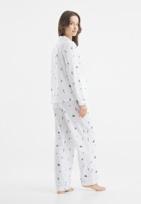 Biała piżama w zestawie z motywem narciarskim i choinki, z długimi rękawami, zapinana na guziki z przodu oraz luźnymi spodniami. Gładki bawełniany materiał.