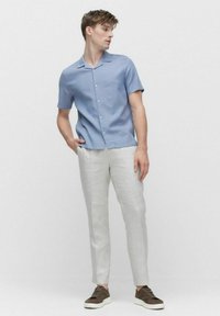 Lichtblauw overhemd met korte mouwen en een knoopsluiting, gecombineerd met lichtgrijze slim-fit broeken en bruine sneakers.