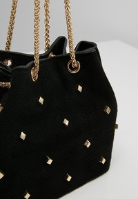 Borsa a secchiello nera in suede con spalline in catena dorata, caratterizzata da borchie quadrate dorate sulla superficie e una finitura testurizzata.