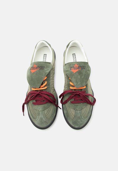 Baskets en daim vert avec des lacets orange et bordeaux, rabat replié affichant un logo rouge, vue de dessus sur fond blanc.