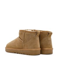 Braune Wildleder-Stiefeletten mit einem weichen Innenfutter, einer flachen Gummisohle und Zugschlaufen an der Rückseite für ein einfaches Anziehen. Schlichtes Design und Textur.