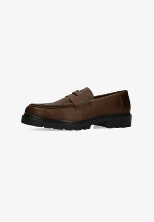 Bruine leren loafer met dikke zwarte rubberen zool en mocassin-stijl stiksels, gezien van opzij tegen een witte achtergrond.