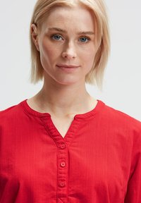 Rotes Button-up-Hemd mit Kragen, aus strukturiertem Stoff und fünf passenden Knöpfen auf der Vorderseite. Einfaches Design, keine Muster.